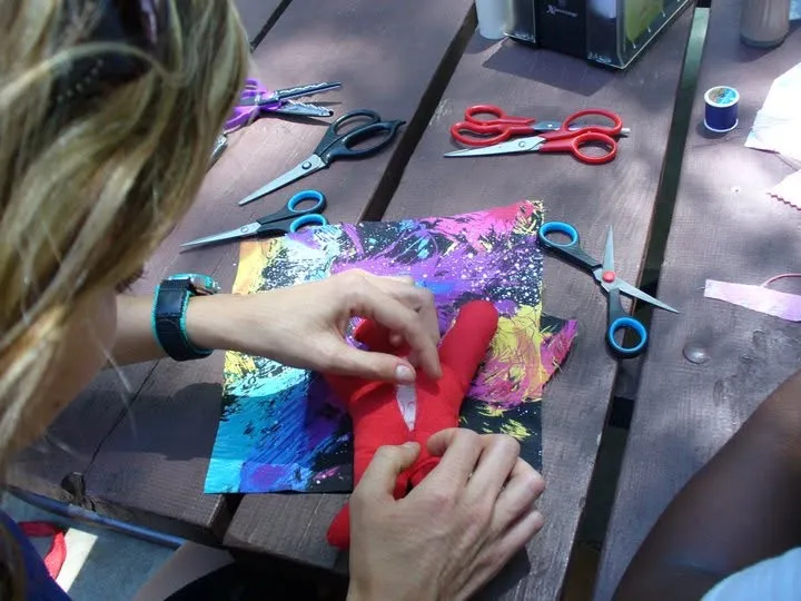 A maker decorating a red cloth doll, surrounded by scissors, thread, and craft materials