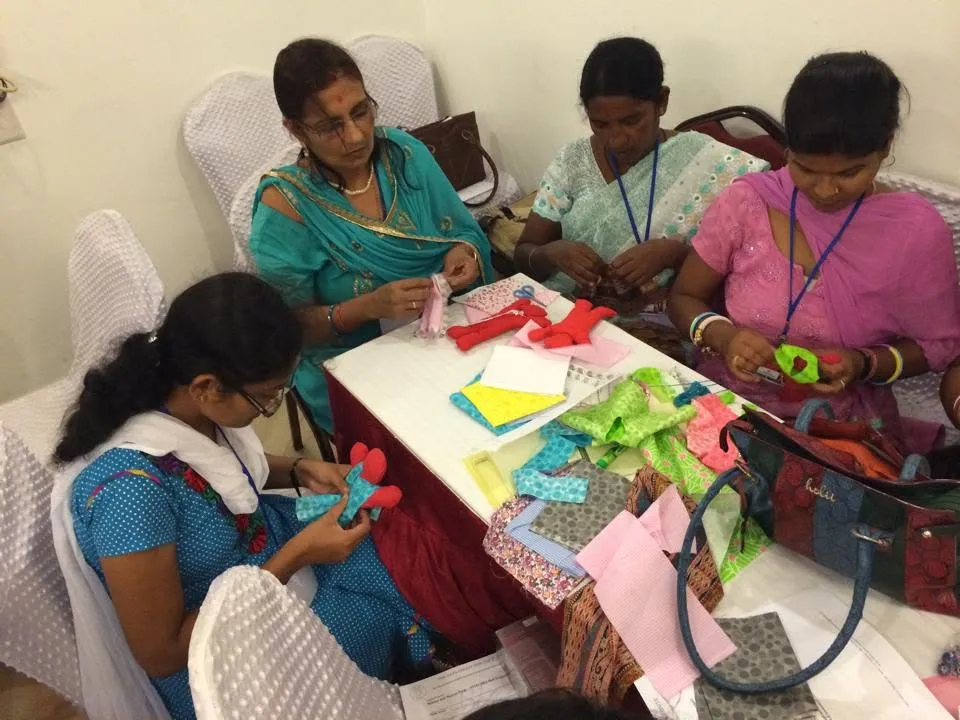 Women in India making cloth dolls together around a table of fabric and supplies